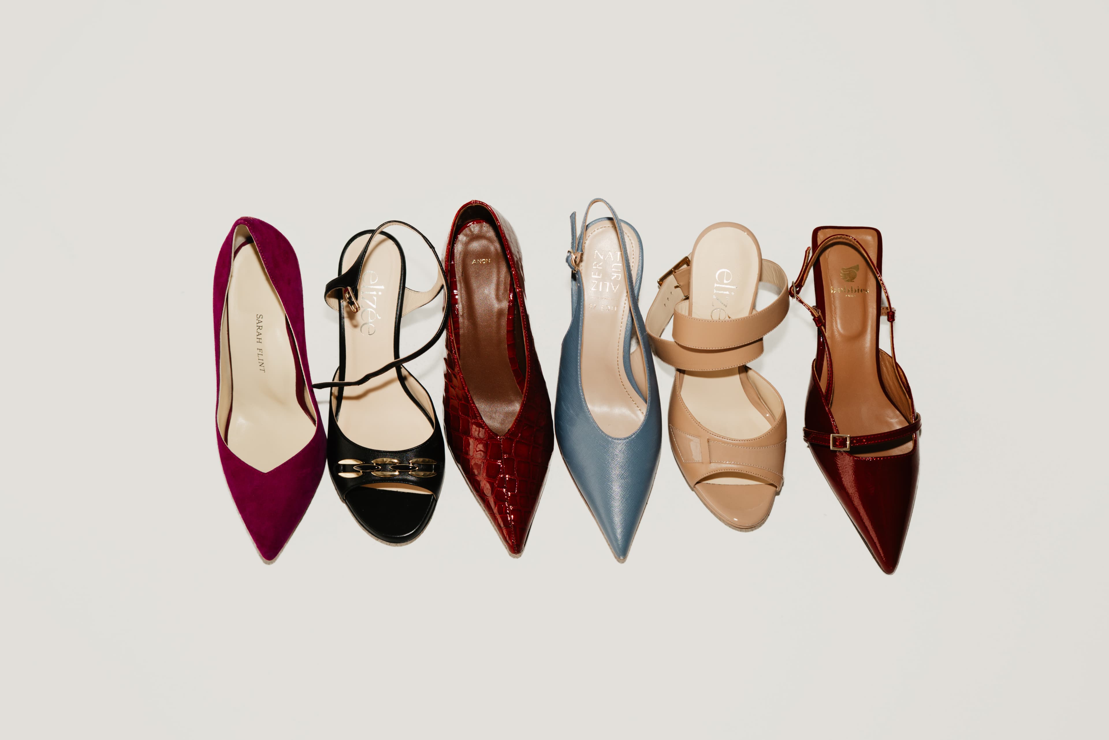 Six pointed heels lined up on a pale backdrop: magenta, black, red patent, powder blue, nude and burgundy