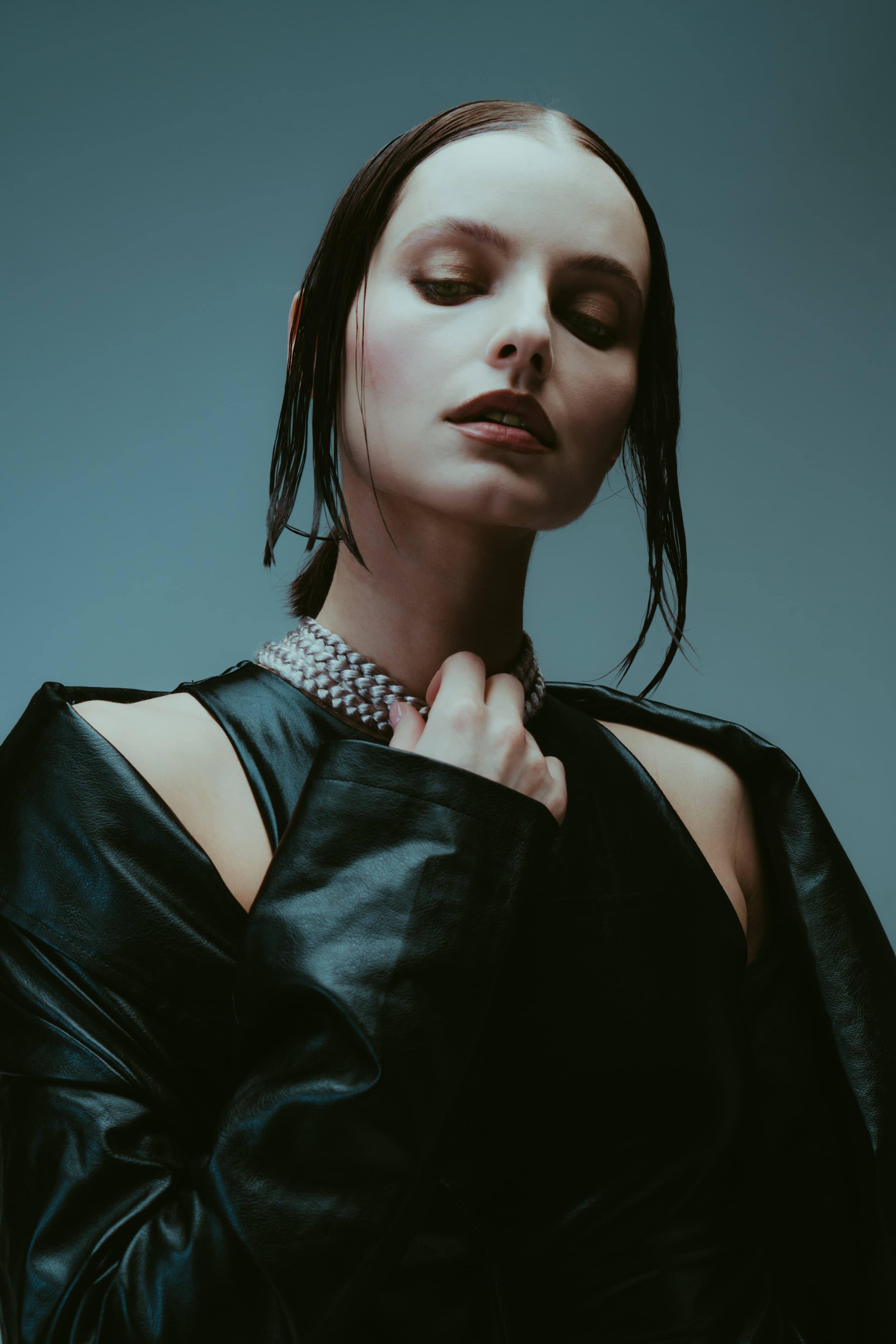 Portrait of a woman with wet-look hair in a black leather jacket and crystal collar, eyes lowered