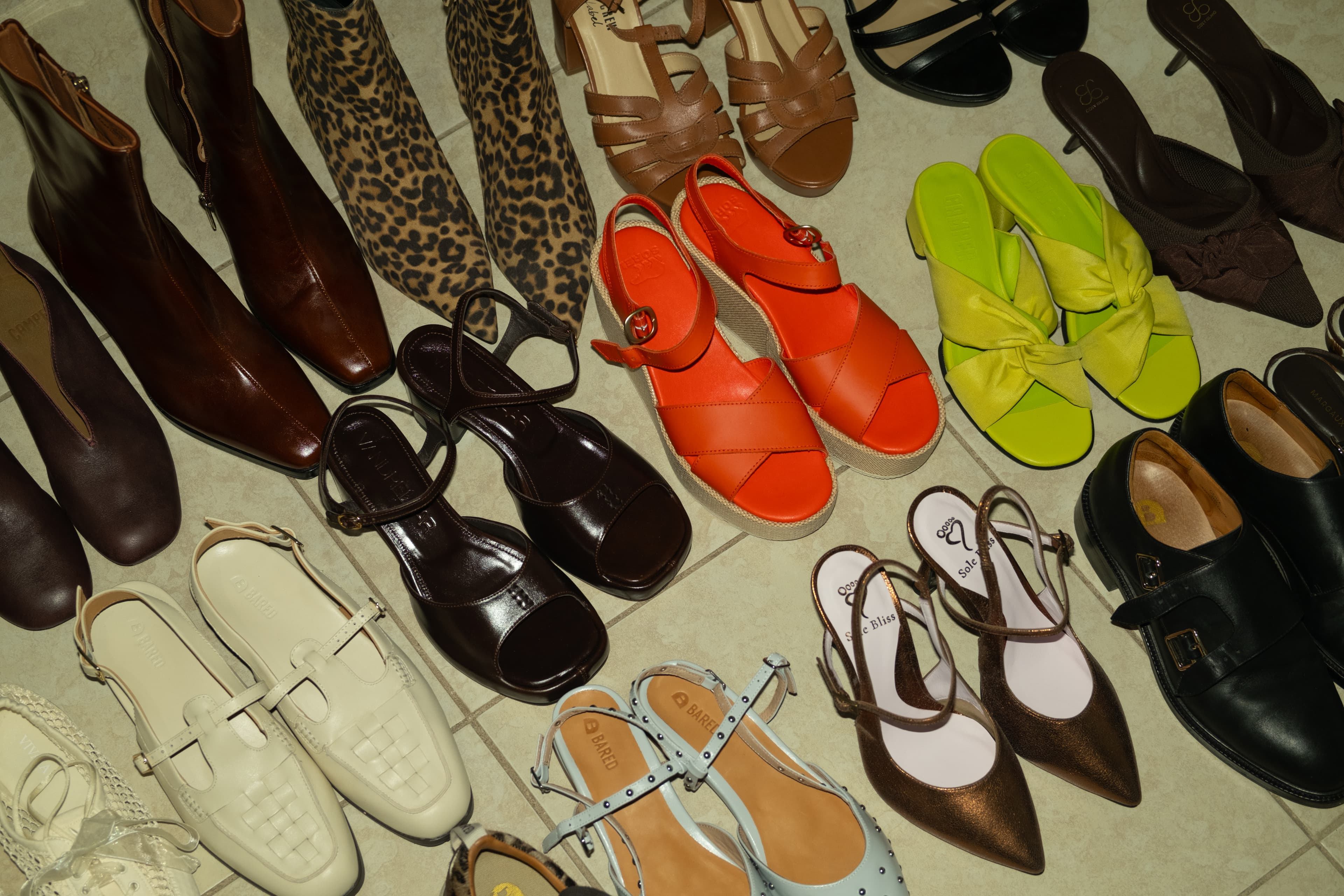 A floor covered in pairs of shoes: brown and leopard boots, orange and lime sandals, cream loafers and studded slingbacks