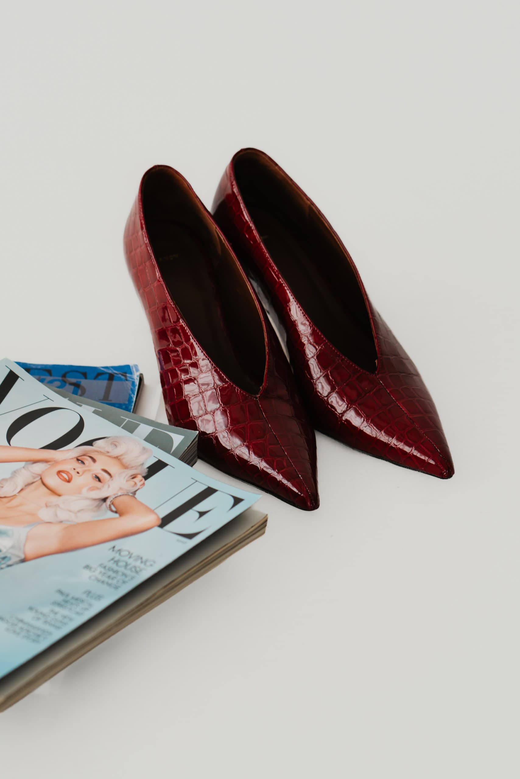 Burgundy croc-effect pointed pumps beside a stack of fashion magazines