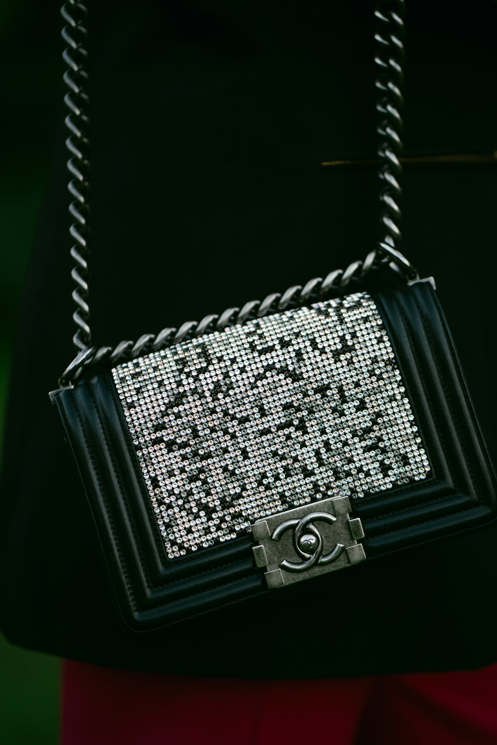 A black flap bag covered in crystals on a chunky silver chain