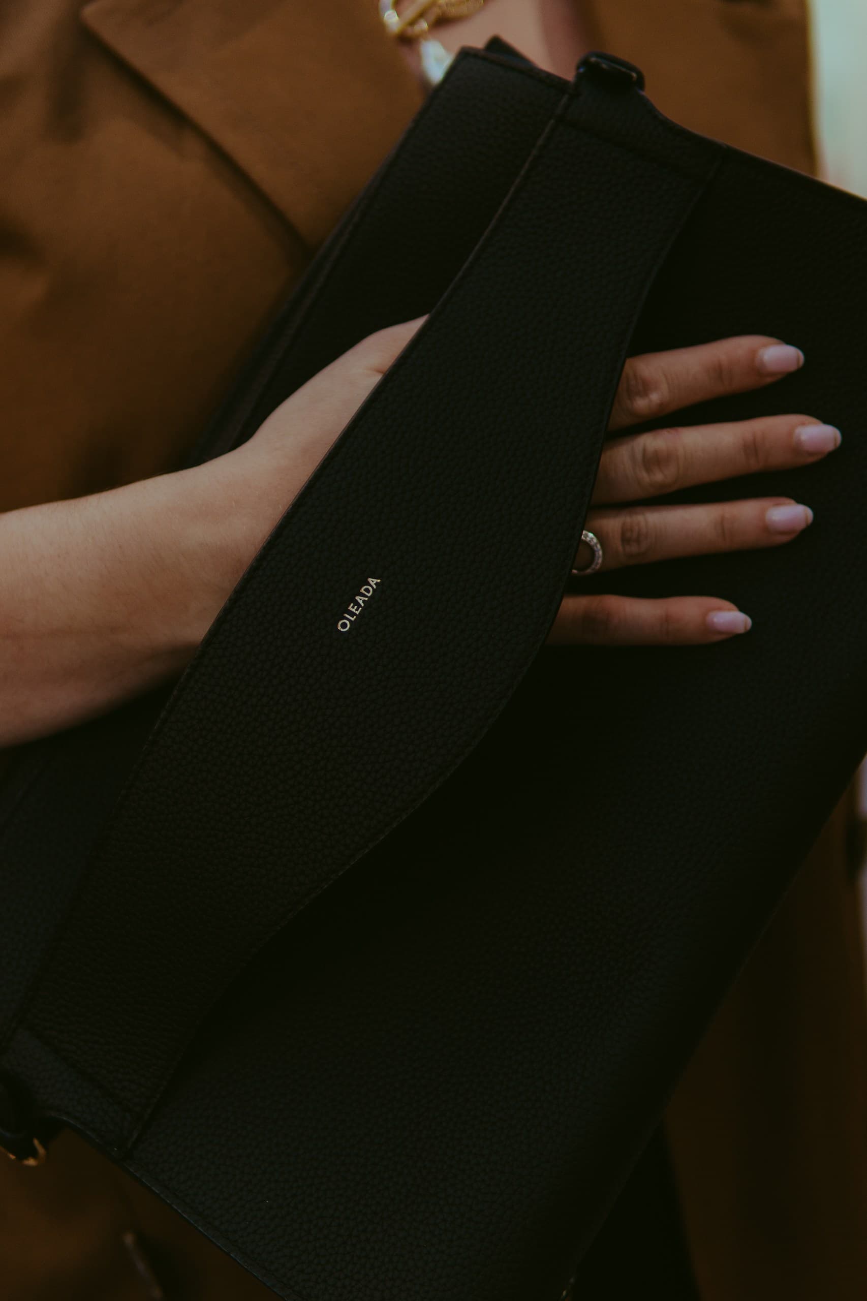 A black leather envelope clutch held against a camel coat