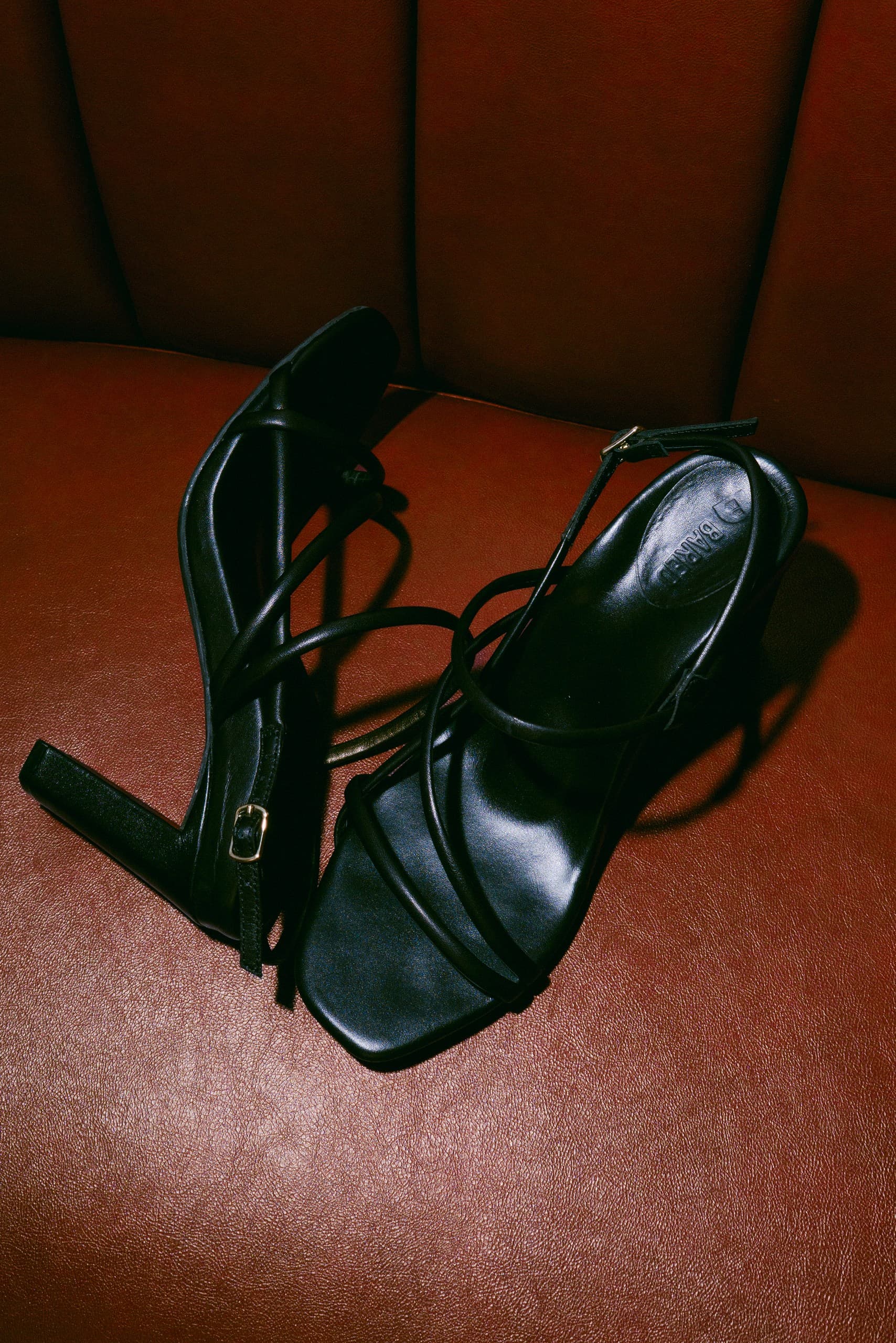 Black knotted strappy sandals lying on a red leather seat