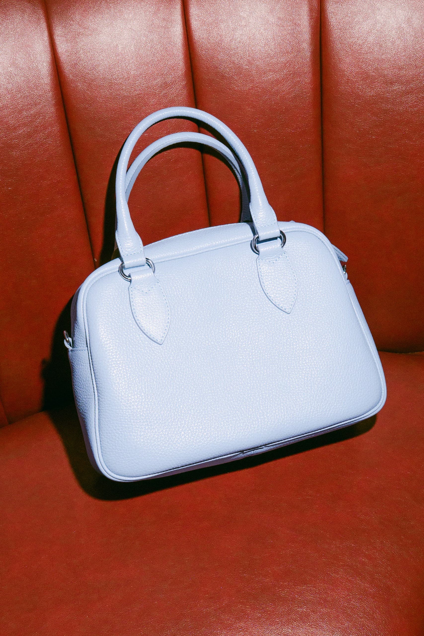 A powder-blue leather bowling bag resting on a red leather seat