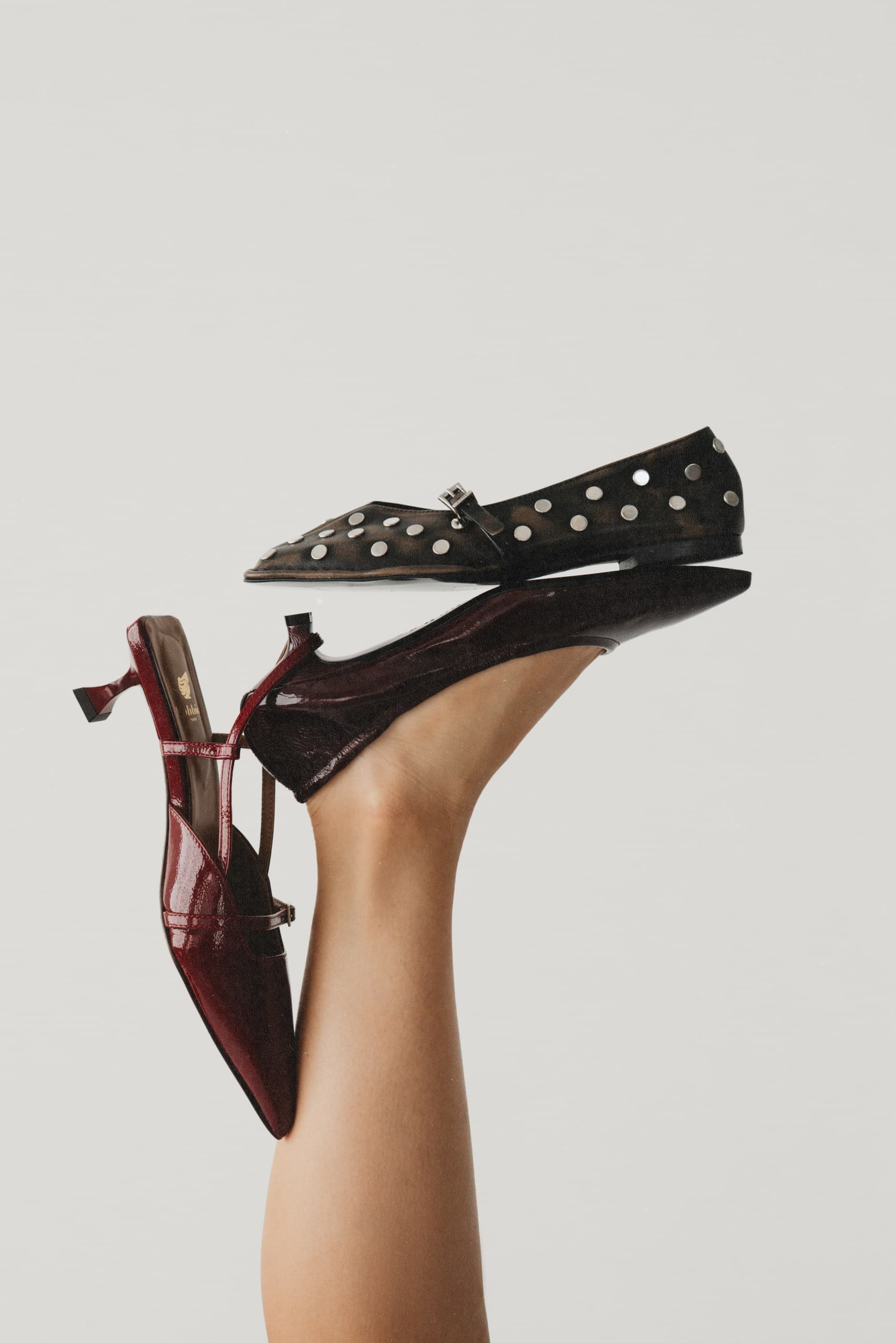 A black studded pointed flat and a burgundy slingback held up on a raised leg