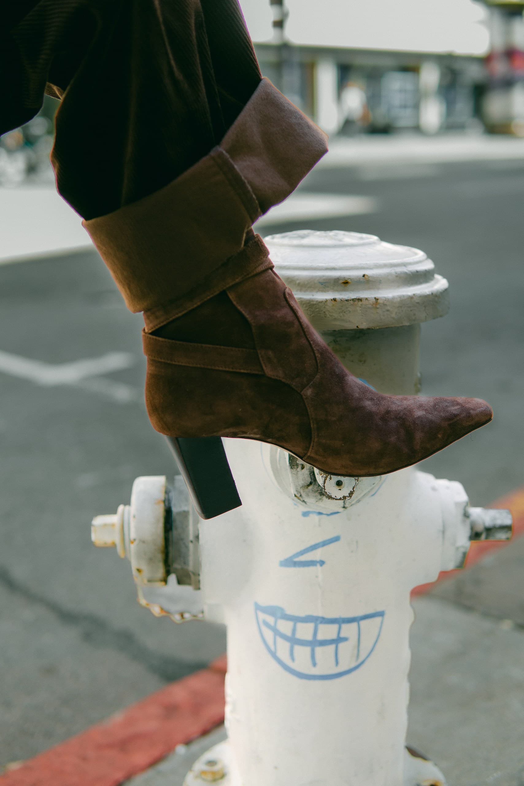 A brown suede slouch boot with a pointed heel resting on a white fire hydrant