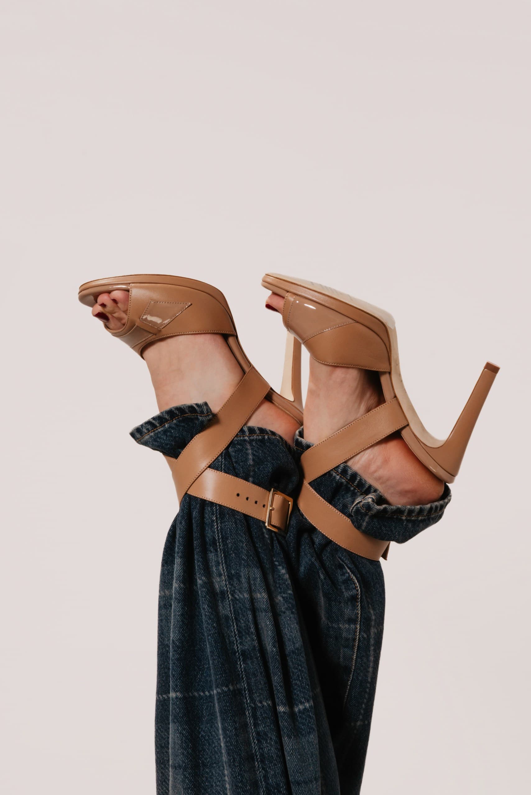 Tan leather strappy heeled sandals on raised feet above dark check trousers