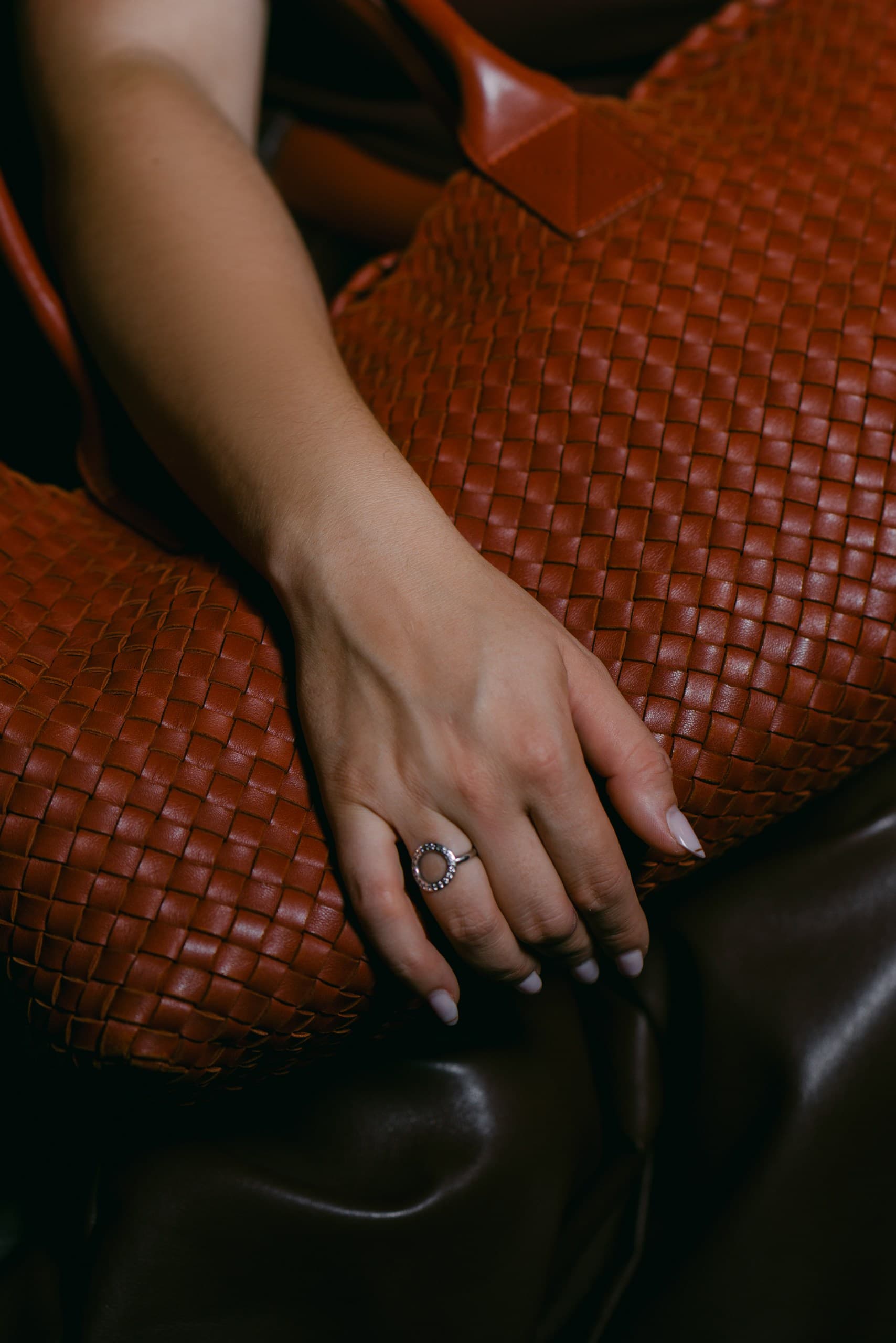 Close-up of a hand with silver rings resting on a cognac woven leather tote